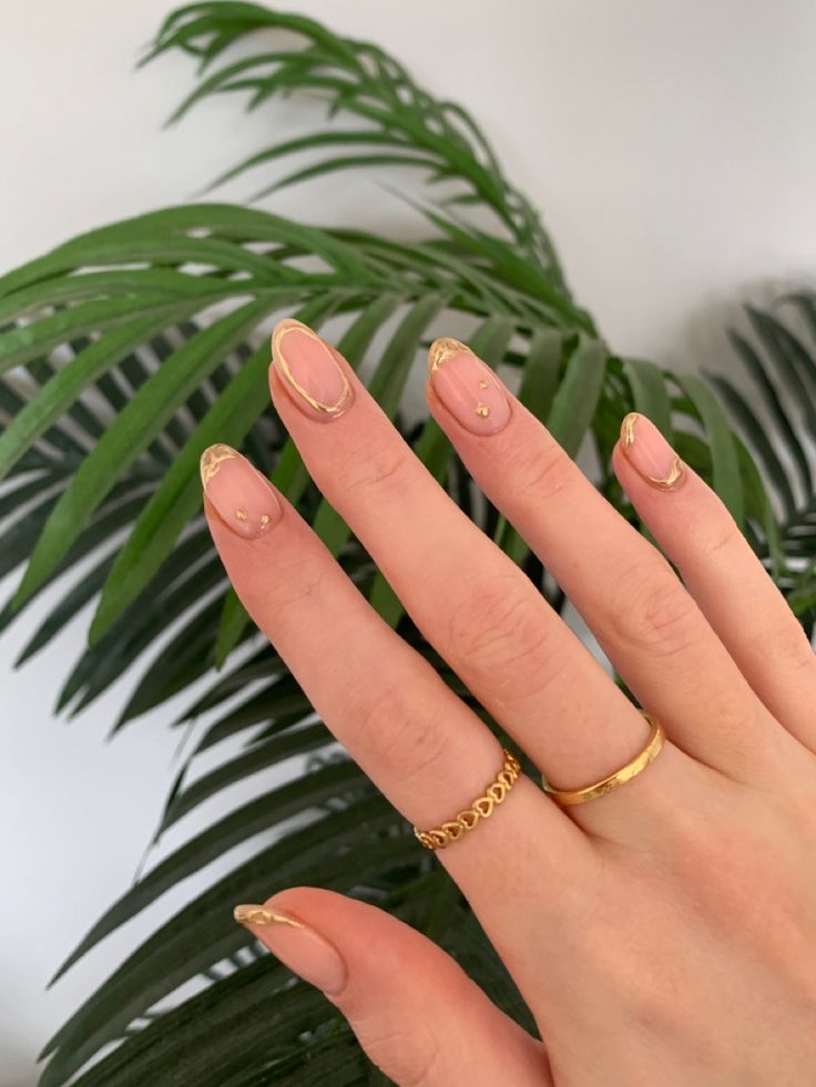 Chic Nude Nail Design with Gold Accents and Minimalist Rings.