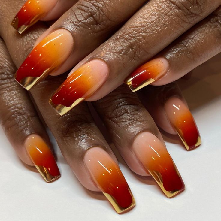 Vibrant Ombre Nail Design: Bold Red to Warm Orange with Glossy Nude Base and Gold Accents.