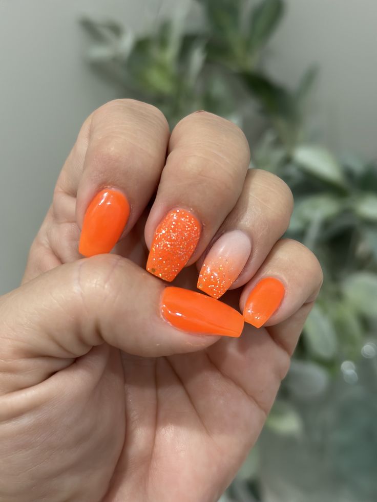 Bold Summer Manicure: Vibrant Orange Nails with Glitter and Ombre Effects.