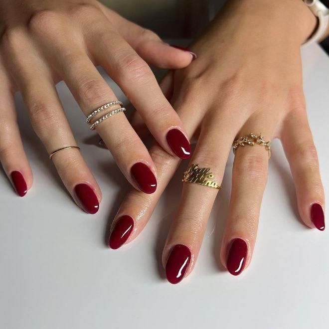 Sophisticated Crimson Almond Manicure with Glossy Finish and Delicate Rings.