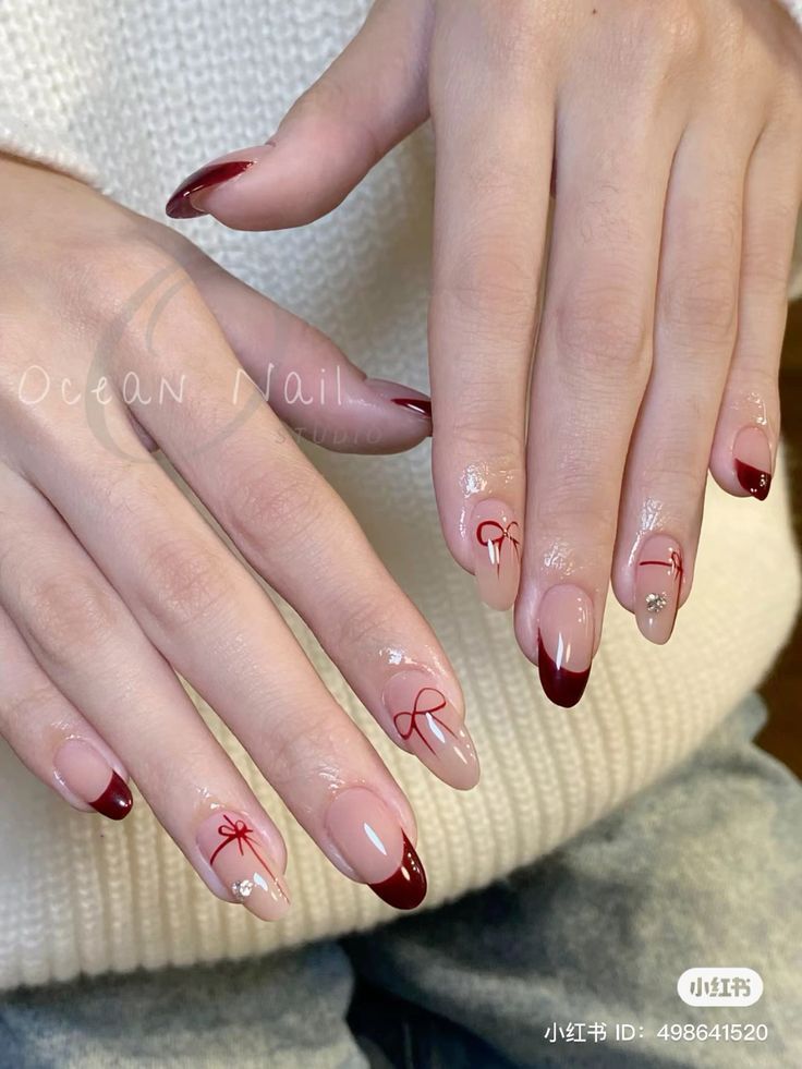 Chic Nail Design: Soft Nude and Deep Burgundy with Hand-Painted Bows and Rhinestone Accents.