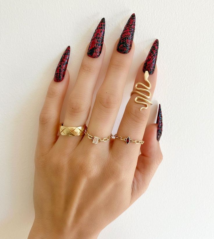 Bold Red and Black Animal Print Stiletto Nails Paired with Elegant Gold and Gemstone Rings for a Chic Fashion Statement.