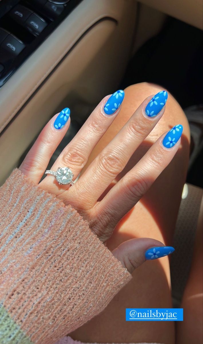 Playful Summer Nail Art: Vibrant Blue with Delicate Flower Designs and Shiny Finish.