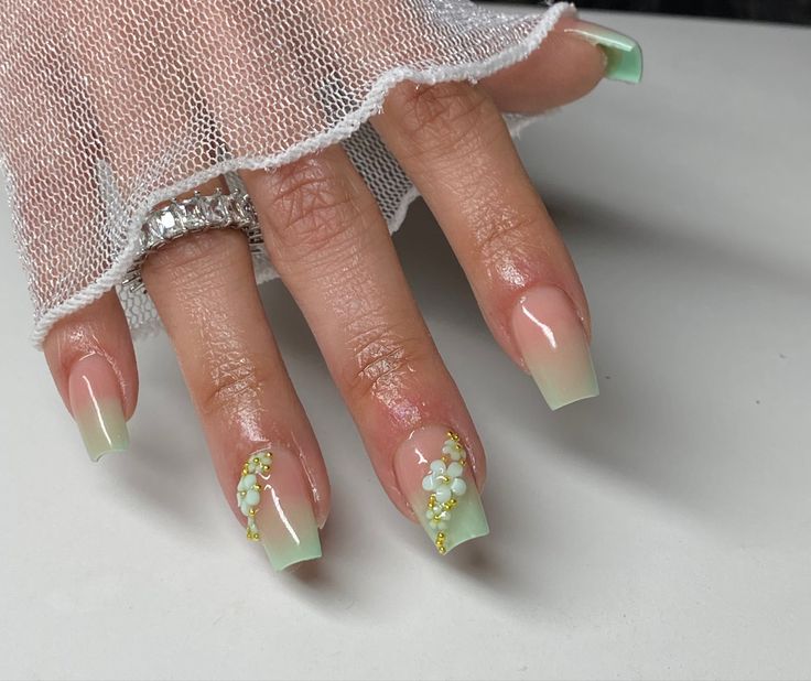 Elegant Ombre Nail Design with Soft Green, Nude Tones, and Floral Embellishments.