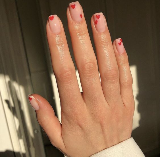 Charming Chic Nail Design with Soft Pink Base and Playful Red Heart Accents.