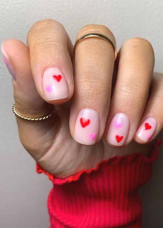 Whimsical Heart Nail Art: Playful Red and Pink Designs on a Soft Nude Base for Expressing Love.