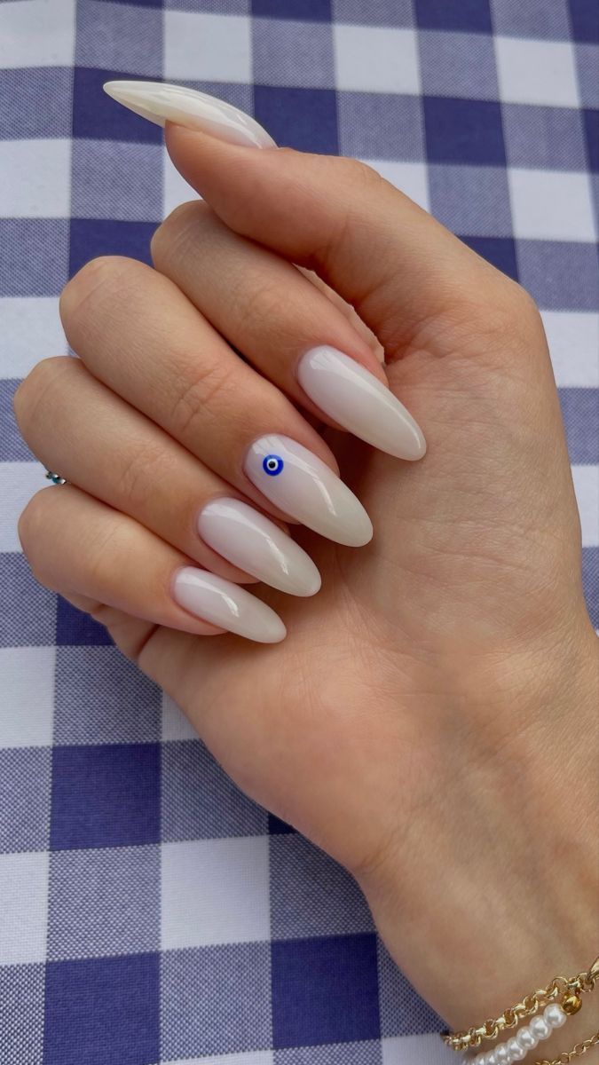 Chic Beige Almond Nails with Delicate Blue Eye Accent for a Subtle Yet Unique Look.