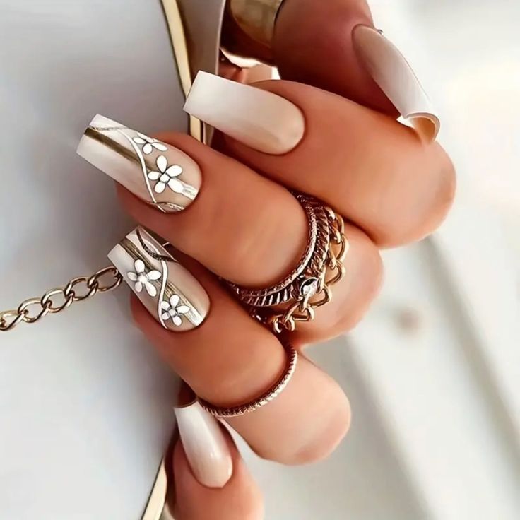 Sophisticated Nail Art: Neutral Tones with Intricate Floral Patterns and Metallic Accents.