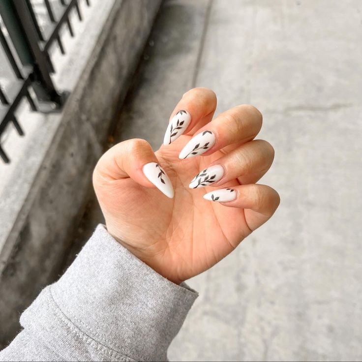 Chic White Stiletto Nails with Delicate Black Floral Designs: A Modern Timeless Elegance.