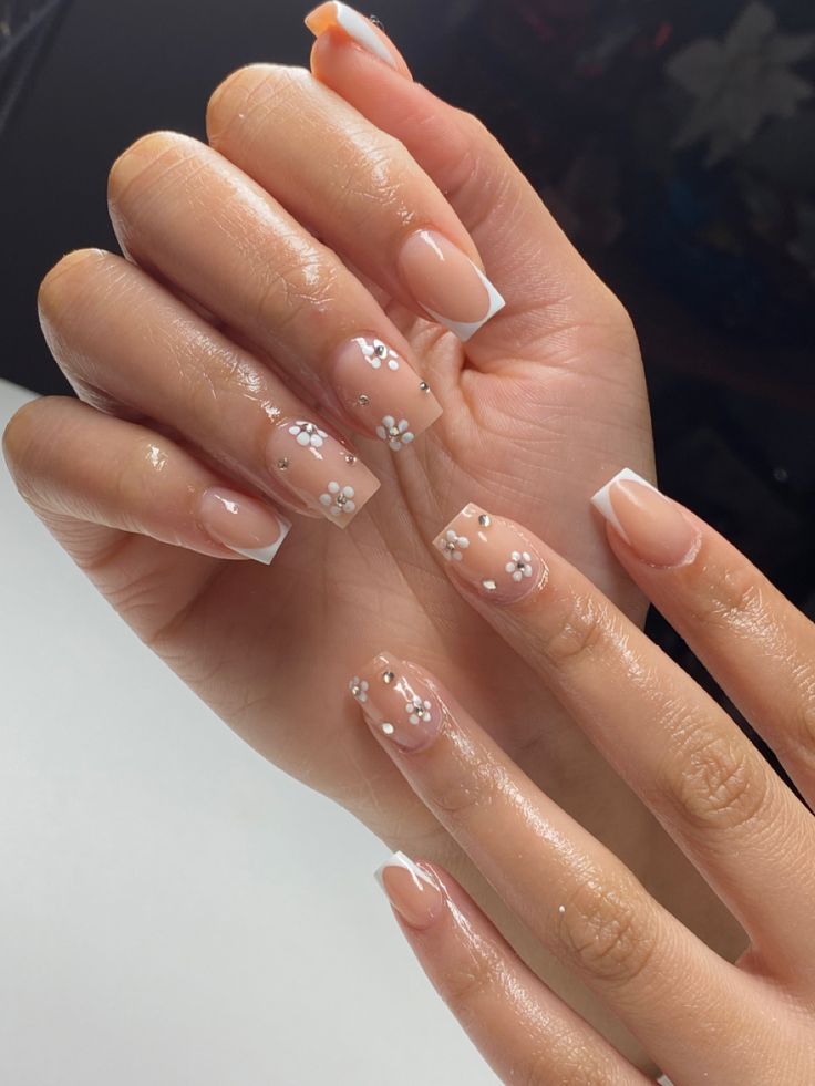 Sophisticated Nail Design with Nude Base, White French Tips, and Floral Accents.