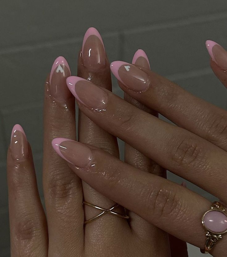 Chic Almond-Shaped Nails: Soft Pink French Tips, Glossy Nude Base, and Elegant Heart Details with Gold Accents.