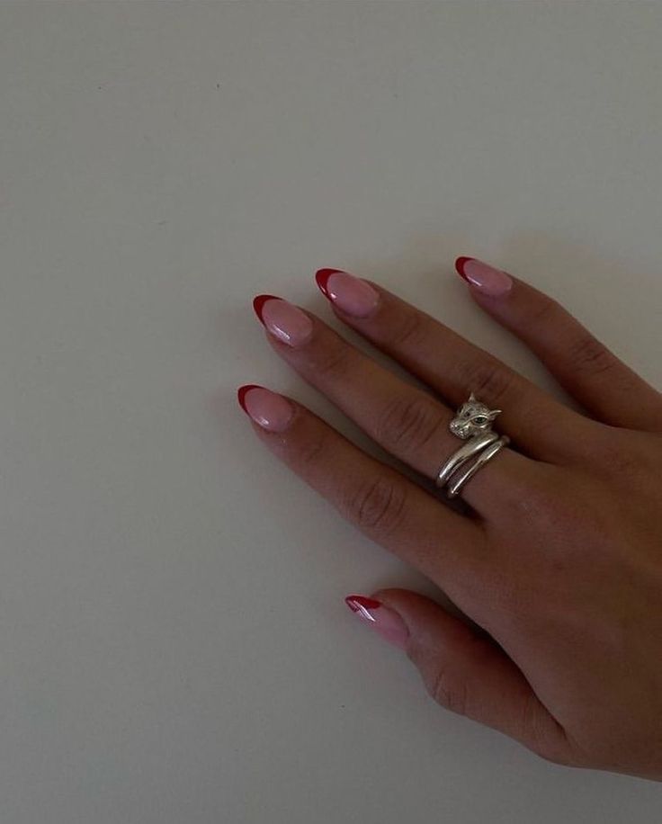 Chic Almond-Shaped French Fade Nails with Soft Pink Base and Red Tips, Enhanced by Stacked Silver Rings.