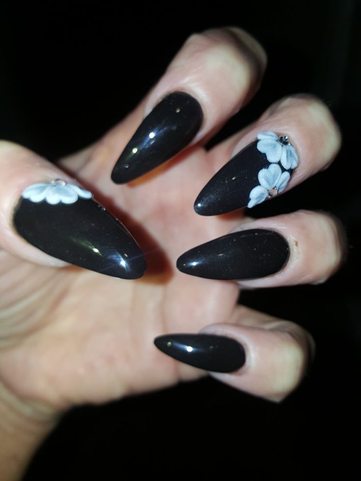 Elegant Black Stiletto Nails with Delicate White Floral Accents: A Striking Contrast of Sophistication and Whimsy.