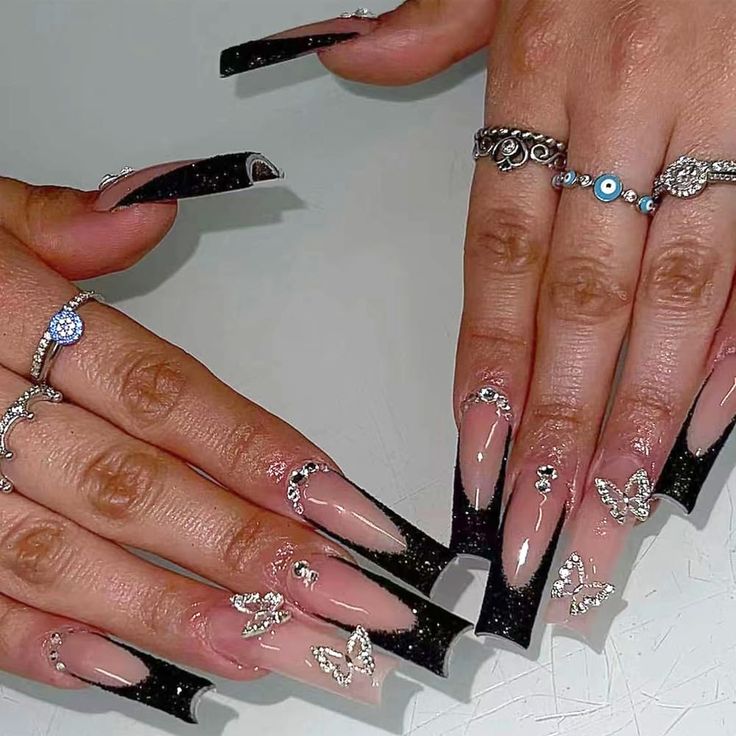 Elegant Black-Tipped Nail Design with Butterfly Accents and Intricate Rings for Glamorous Occasions.