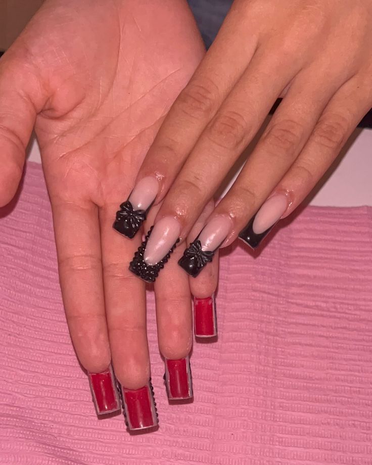 Striking Nail Design: Bold Red Meets Elegant Nude with Intricate Black Embellishments.