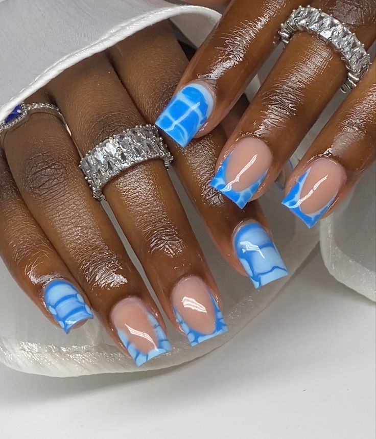 Chic Bold Nail Design: Soft Nude and Vibrant Blue with Artistic Wave Patterns.