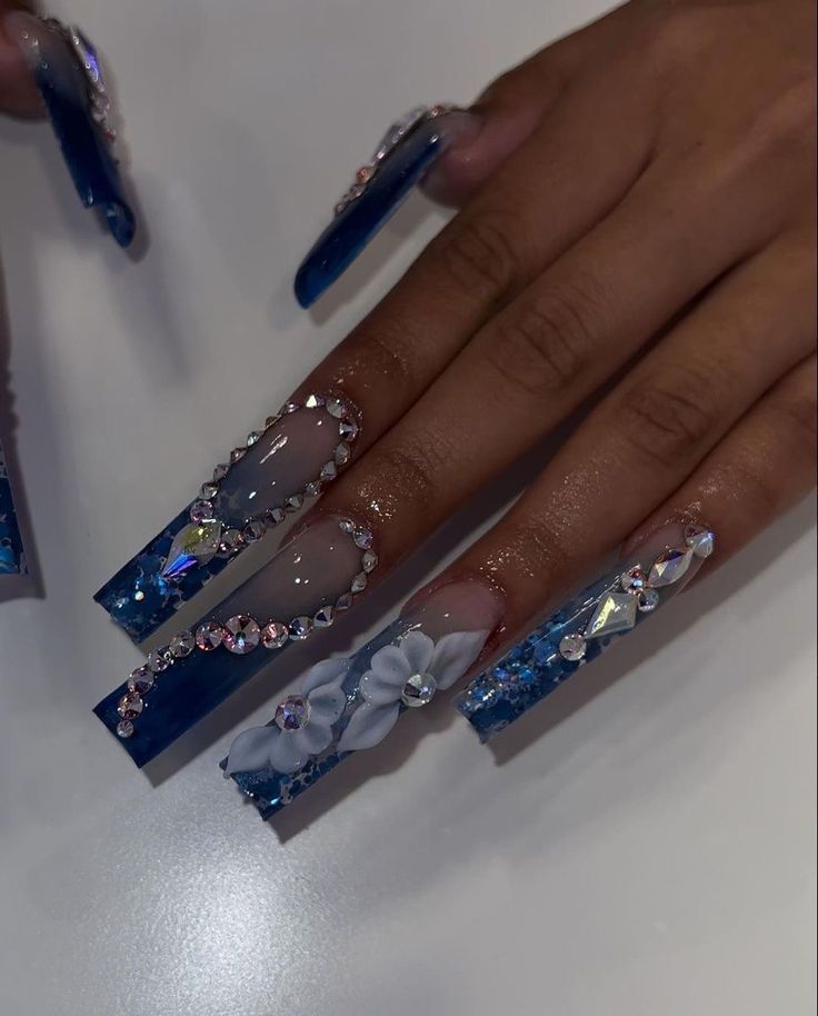 Vibrant Blue Gradient Nail Art with 3D Floral Accents and Sparkling Rhinestones for a Bold Statement.