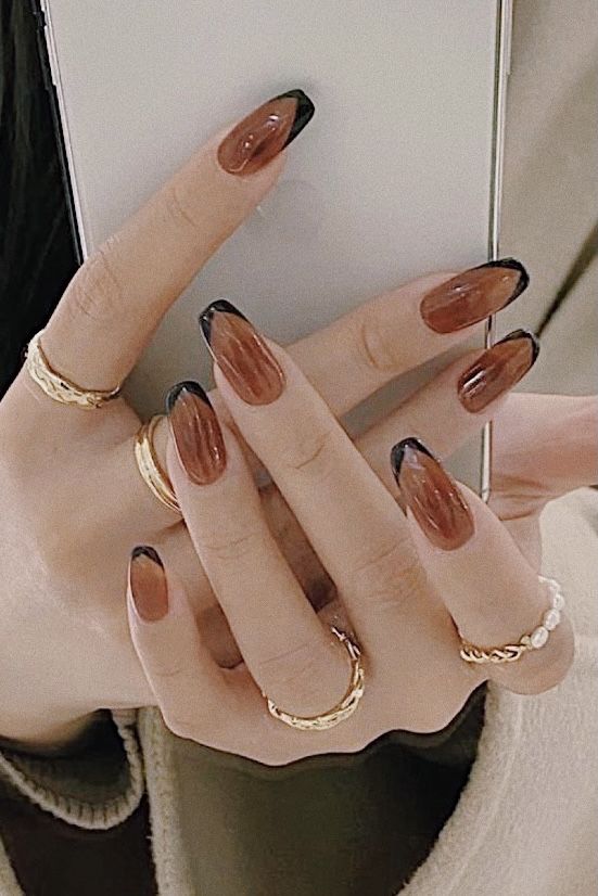 Chic Almond-Shaped Nail Design: Glossy Brown Base with Bold Black Tips and Gold Accents.