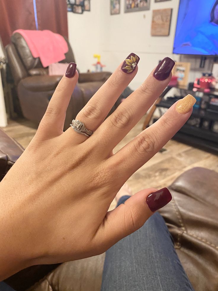 Elegant Deep Burgundy and Gold Nail Design with Floral Accent