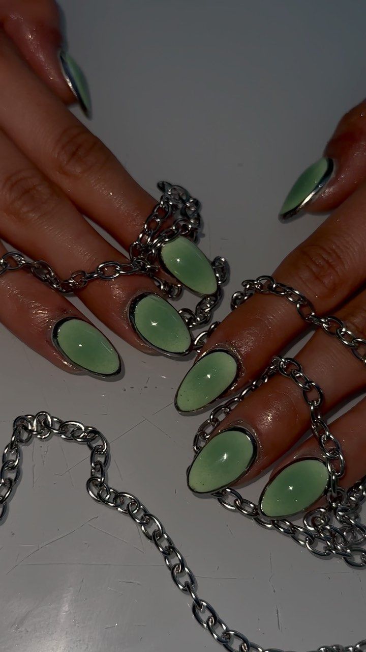 Chic Almond-Shaped Nails in Soft Green with Bold Black Outlines and Layered Silver Chains.