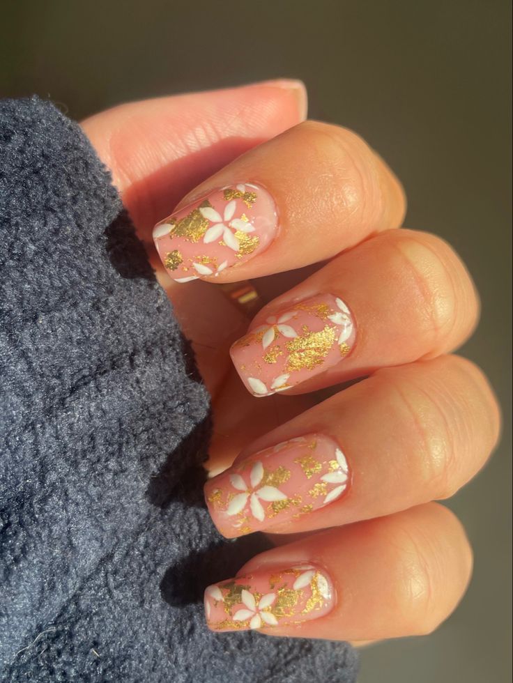 Delicate Floral Nail Design with White Flowers and Gold Accents on a Soft Pink Base.