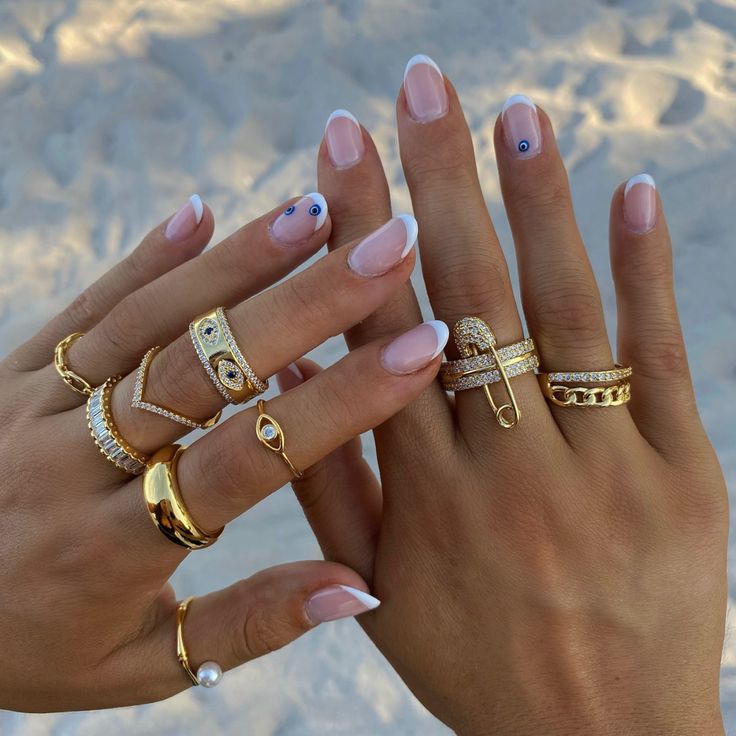 Chic French Manicure with Glamorous Statement Rings and Decorative Touches.