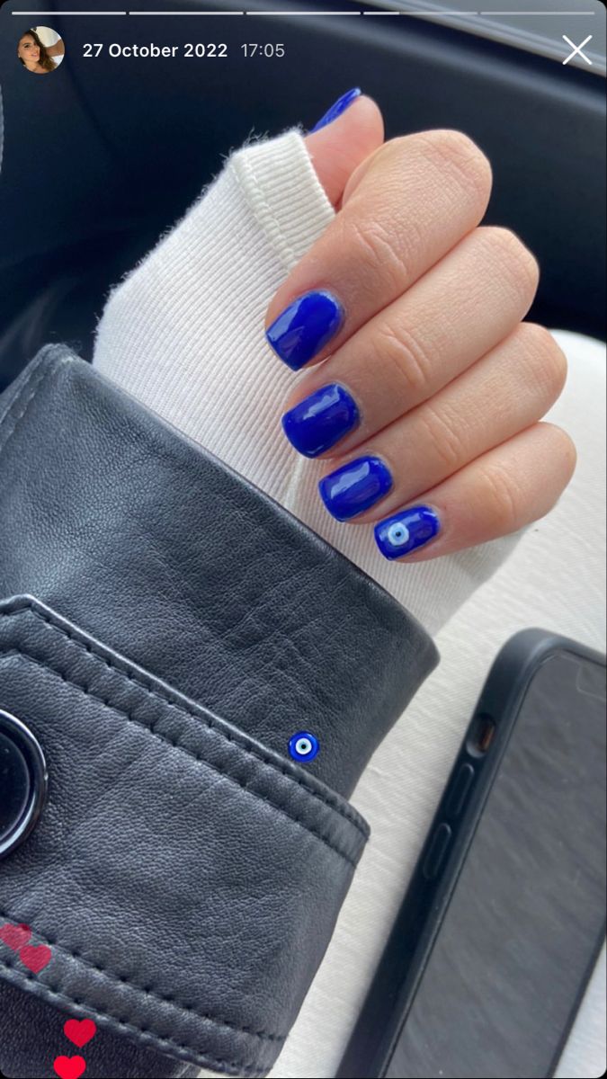 Chic Nail Art: Bold Blue Nails Contrast with Sweater's Soft Tones and Playful Eye Motifs.