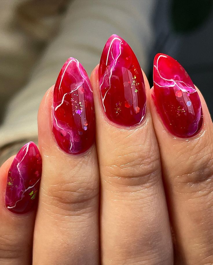 Bold Stiletto Nail Design: Vibrant Red with Marbled Pink and Glitter Accents.