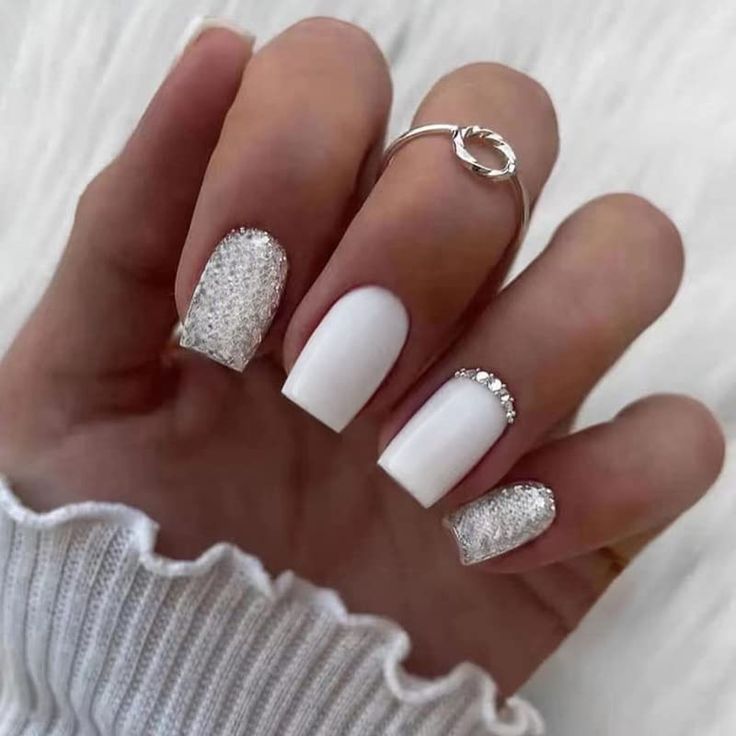 Chic Matte White Nail Design with Glitter Accents and Silver Ring Accessories.