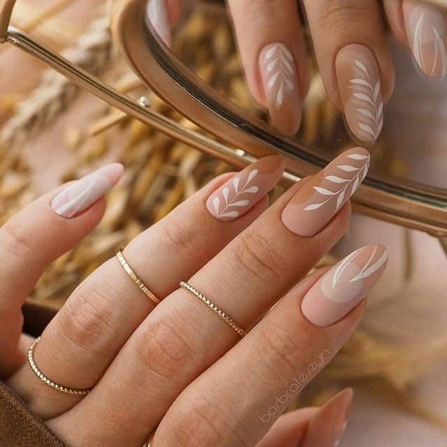 Chic Elegant Nail Design with Soft Nude Base and Delicate White Leaf Patterns Accented by Thin Gold Rings.