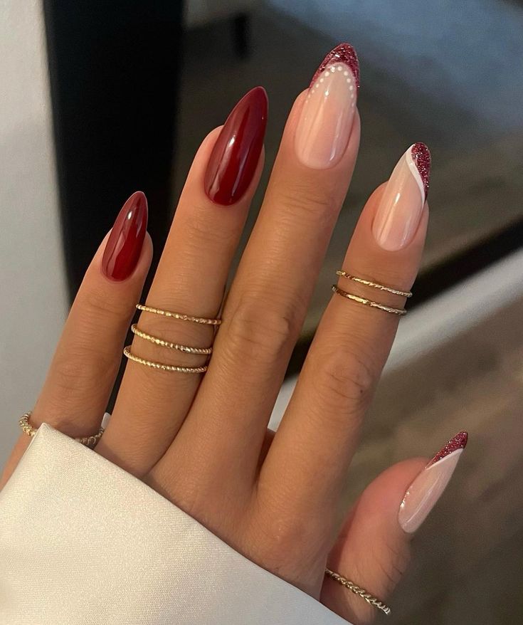 Sophisticated Almond-Shaped Nail Design: Bold Red, Soft Nude, and Glitter Accents with Elegant Gold Ring Accessories.