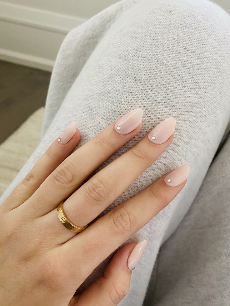 Elegant Glossy Nude Nail Design with Gemstone Accents and Minimalist Gold Ring.