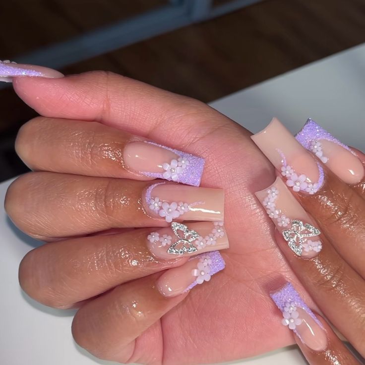 Elegantly Designed Nails with Soft Nude and Pastel Purple Hues, Floral Accents, and Shimmering Details.