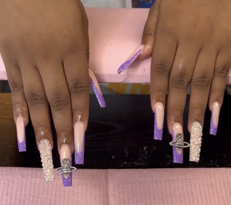 Sophisticated Stiletto Nail Design: Soft Nude to Vibrant Purple Gradient with Glitter and Rhinestone Accents.