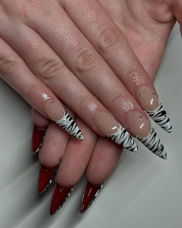 Chic Almond-Shaped Nails: Classic Nude and Bold Red with Zebra Patterns and Sparkling Gems.