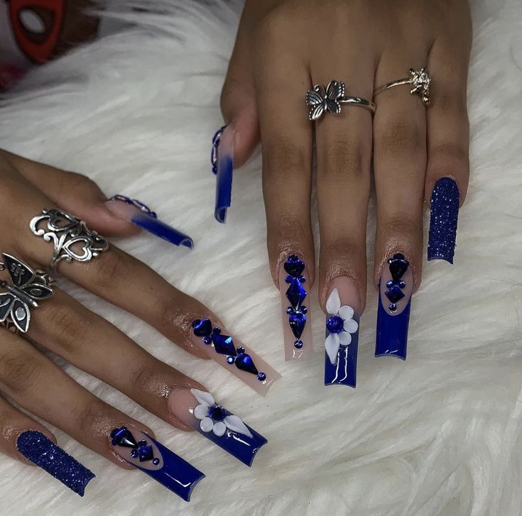 Elegant Nail Design: Vibrant Blue Palette with Glossy and Matte Finishes, Floral Accents, and Sparkling Gems on Long Coffin-Shaped Nails.