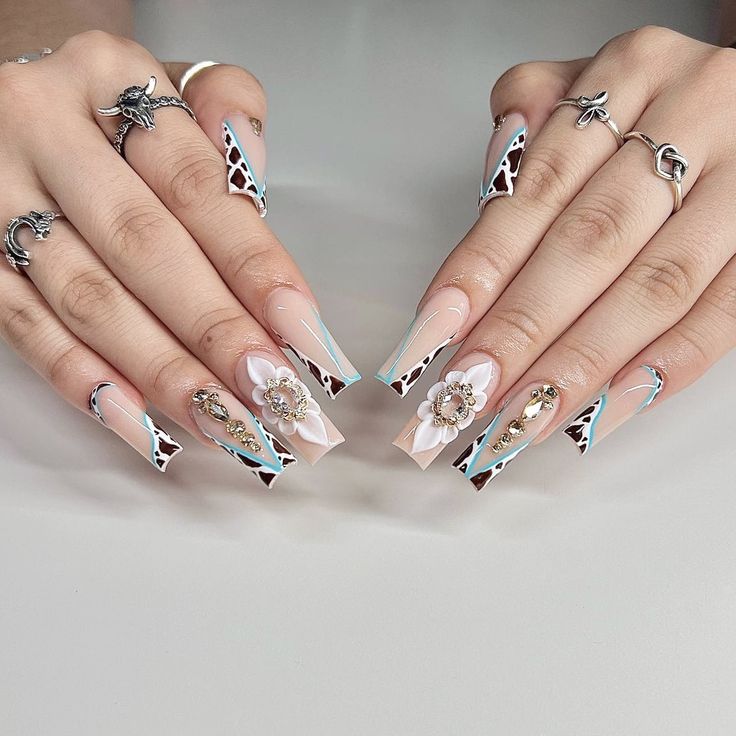 Chic Elongated Nail Design with Nude and Pastel Hues Accented by Floral Embellishments and Stylish Rings.