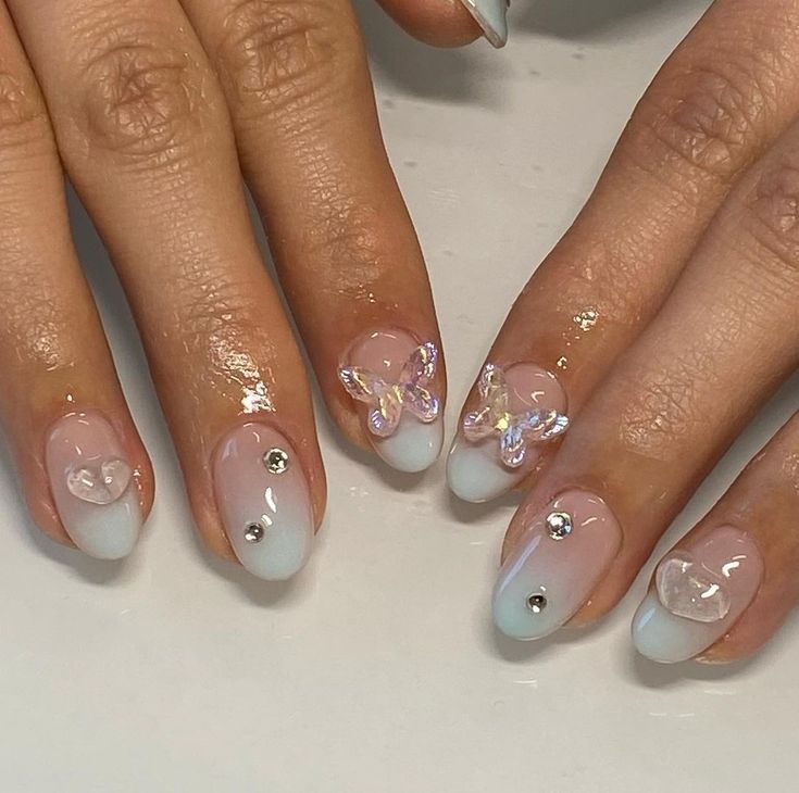 Charming Pale Blue and Nude Gradient Nail Design with 3D Butterfly, Heart Accents, and Sparkling Rhinestones.