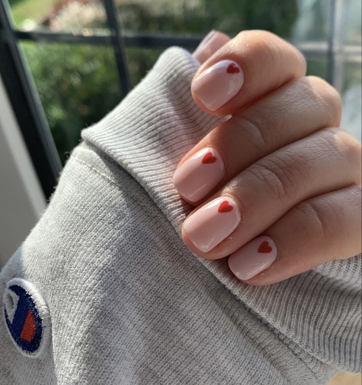 Charming Heart-Themed Nail Design: Soft Pink Base with Playful Red Hearts.