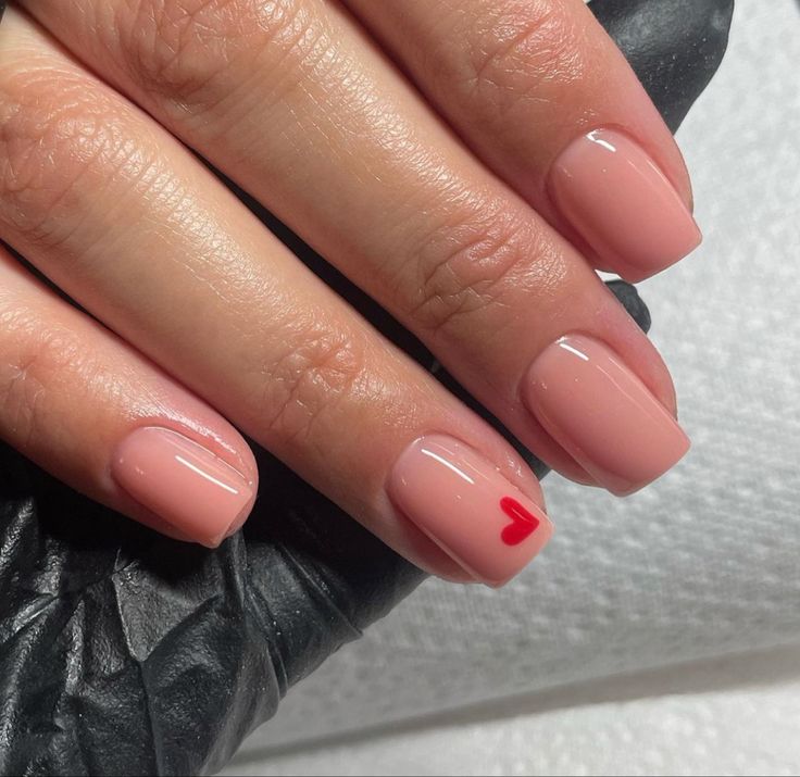 Chic Nude Nail Design with Playful Red Heart Accent.