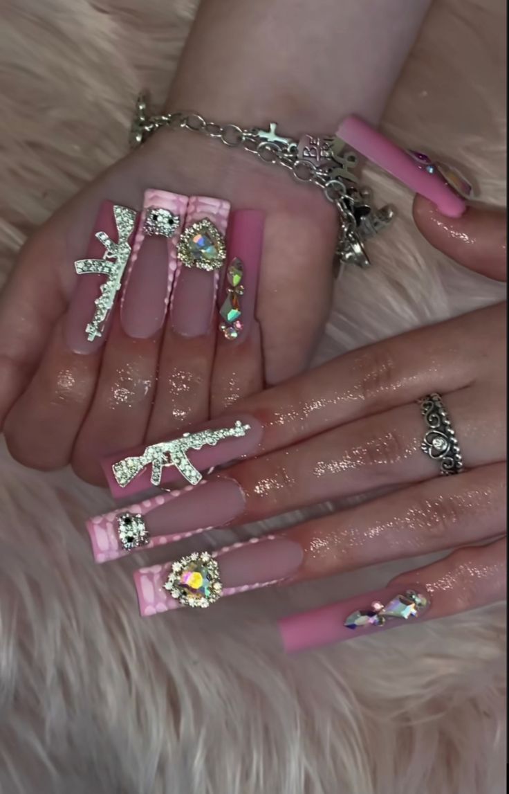 Glamorous Long Pink Acrylic Nails with Edgy Gun Motifs and Dazzling Embellishments.