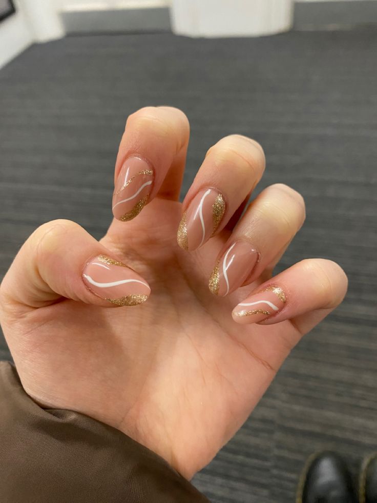 Sophisticated Nude Nail Design with Gold Glitter Tips and Elegant Swirling Lines.