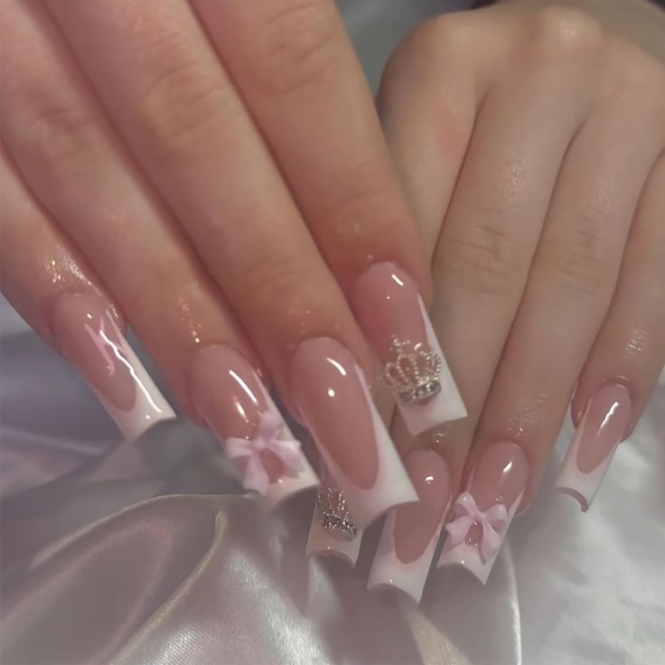 Elegant French Tip Nail Design with Bows and Sparkling Crown Embellishments in Soft Pink and White.