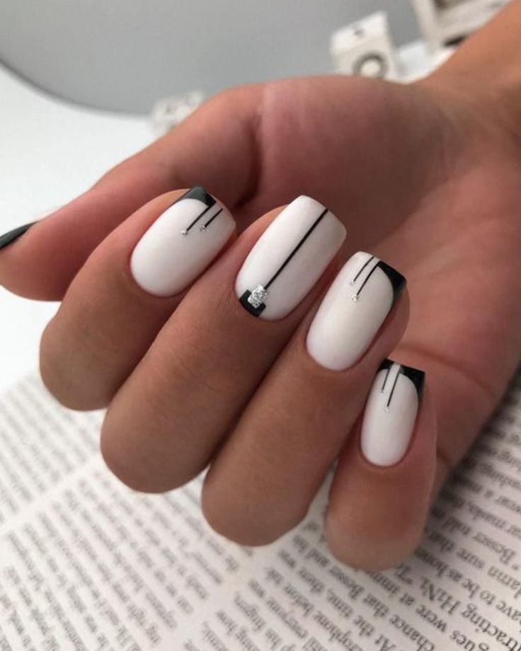 Chic White and Black Nail Design with Artistic Lines and Rhinestone Accent.