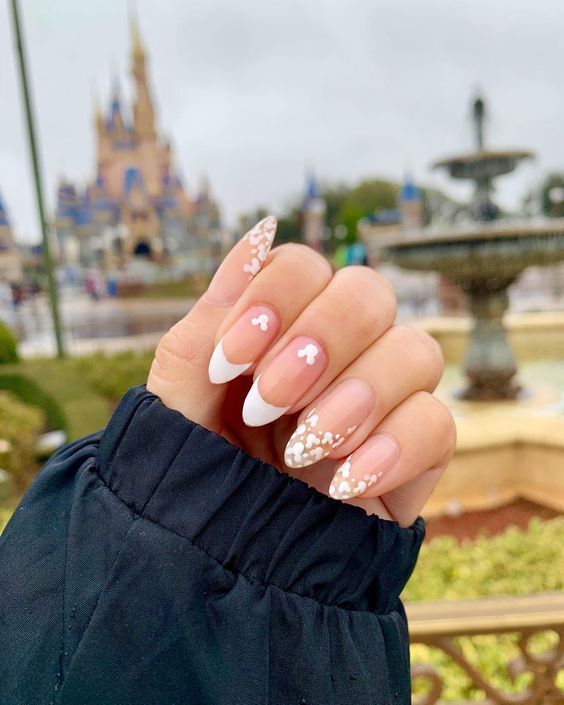 Whimsical Romantic Nail Design: Nude Base with White Tips, Heart Accents, and Shimmering Glitter.