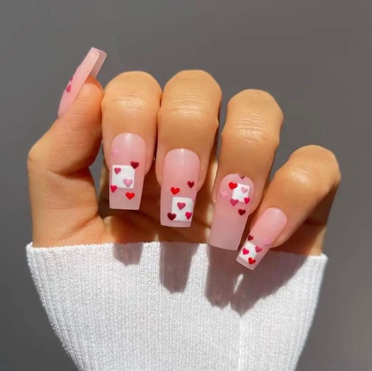 Whimsical Soft Pink Nail Design with Playful Red and White Heart Patterns