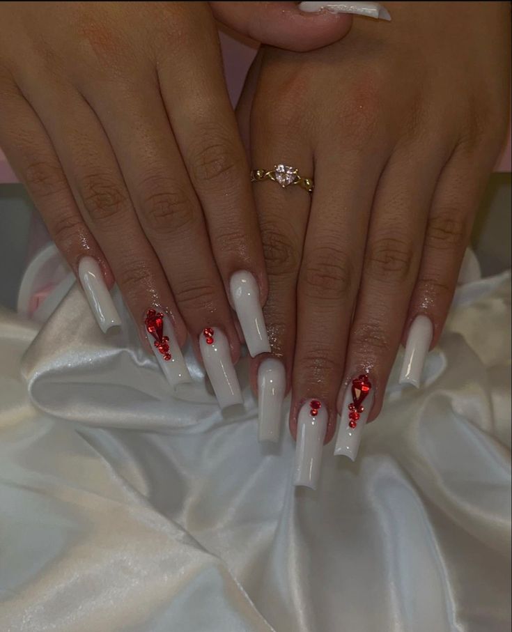 Chic White Nails with Red Accents and Glamorous Gemstone Appliques for a Trendy Look.