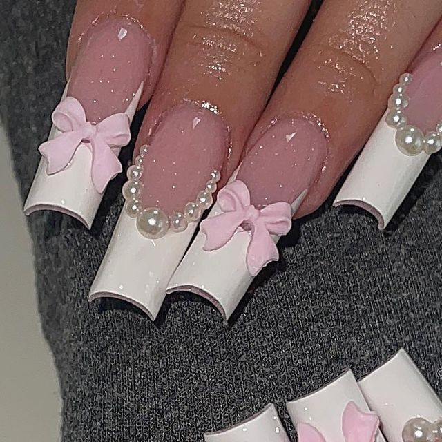 Chic Nail Design: Glossy White Tips with Soft Pink Base, Bows, and Pearl Accents.