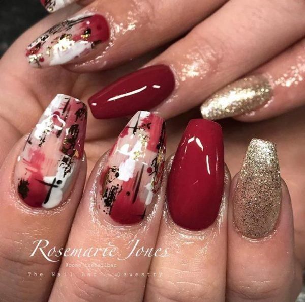 Glamorous Deep Red and Gold Nail Design with Abstract Patterns and Shimmering Accents.