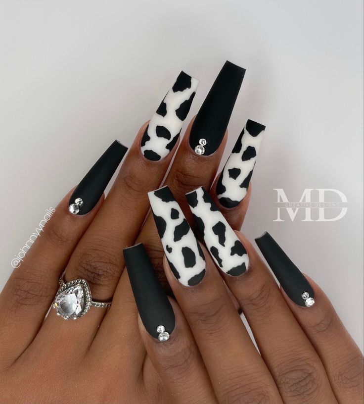 Chic Cow Print and Matte Black Nail Design with Rhinestone Accents.